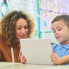 Young child on laptop sat next to teacher